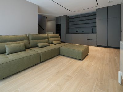 Canapé modulaire vert olive dans un espace de vie ouvert avec carrelage imitation bois clair. Meubles intégrés gris foncé avec évier et étagères en arrière-plan.