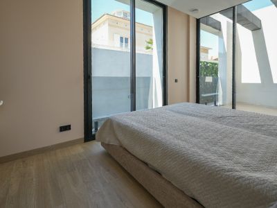 Chambre lumineuse avec parquet clair et grandes baies vitrées coulissantes à cadre noir, offrant une vue sur une maison voisine et un mur végétal extérieur.