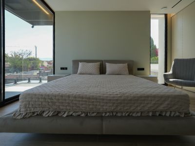 Chambre principale avec lit flottant, tête de lit rembourrée, grandes fenêtres avec vue sur la mer et fauteuil. Tables de chevet intégrées.