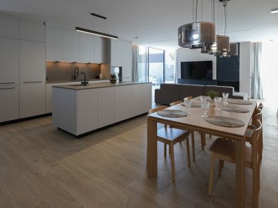 Cuisine design minimaliste avec îlot central et robinetterie noire, ouverte sur une élégante salle à manger en bois avec six chaises et suspensions modernes.