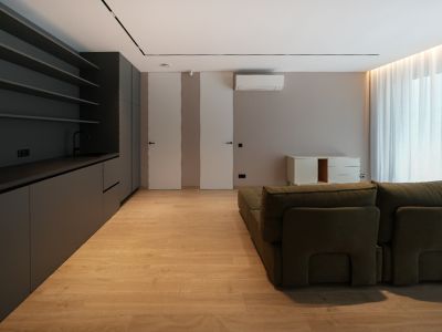 Espace de vie moderne avec kitchenette intégrée gris foncé, sol imitation bois clair et canapé modulaire vert. Portes affleurantes et lumière naturelle.