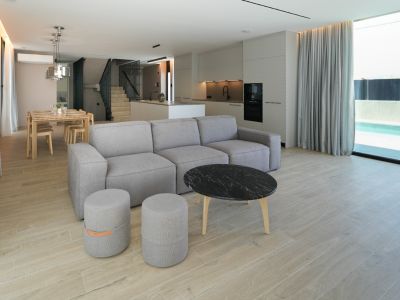 Espace de vie ouvert avec canapé modulaire, table basse en marbre et cuisine intégrée, offrant une vue sur la piscine extérieure via de grandes baies vitrées.