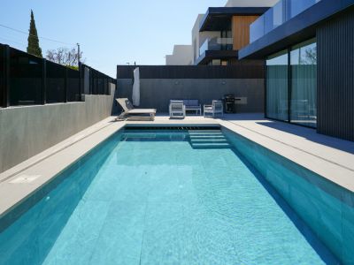 L'espace extérieur comprend une piscine rectangulaire aux carreaux bleus clairs et marches, bordée d'un dallage gris clair. Un salon de jardin moderne et une chaise longue invitent à la détente près de la façade épurée.