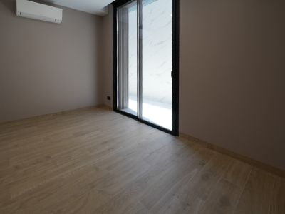 Pièce vide avec carrelage imitation bois clair, murs taupe et grande porte coulissante vitrée noire. Une unité de climatisation murale est présente.
