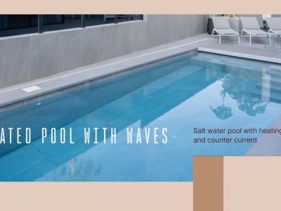 Piscine d'eau salée chauffée avec système de nage à contre-courant et escaliers, entourée de carrelage gris et transats.