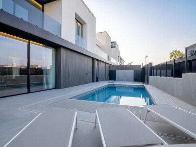 Piscine extérieure à l'eau bleue, entourée d'une terrasse carrelée grise et de platelage composite. Façade moderne avec de grandes baies vitrées reflétant le ciel.