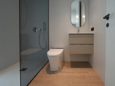 Salle de bain contemporaine avec douche à l'italienne en verre fumé et mur texturé gris, WC suspendu design, meuble vasque flottant et carrelage imitation bois clair.