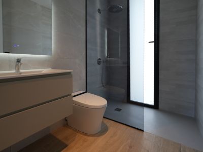Salle de bain contemporaine avec meuble-lavabo suspendu, miroir éclairé, WC mural et douche à l'italienne avec pommeau pluie, murs carrelés gris et sol effet bois.