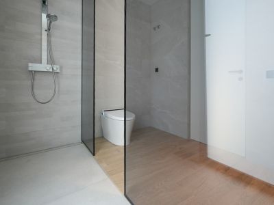 Salle de bain moderne avec douche à l'italienne, carrelage gris clair et mitigeur thermostatique chromé. Une paroi vitrée sépare la douche des toilettes intelligentes avec carrelage imitation bois.