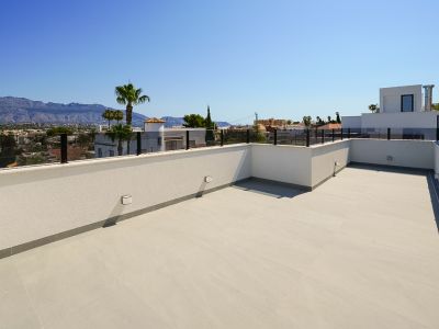 Vaste terrasse sur le toit avec carrelage clair et garde-corps en verre moderne, offrant des vues panoramiques sur les montagnes et la ville.