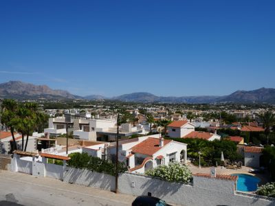 Vue aérienne du quartier résidentiel d'Albir, avec son architecture variée, une végétation luxuriante et une piscine privée, encadrée par les montagnes sous un ciel bleu clair.