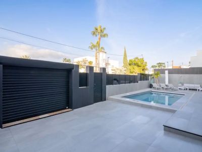 Vue extérieure de la piscine privée, du patio carrelé gris clair et du portail de garage sombre avec accès piéton sécurisé.