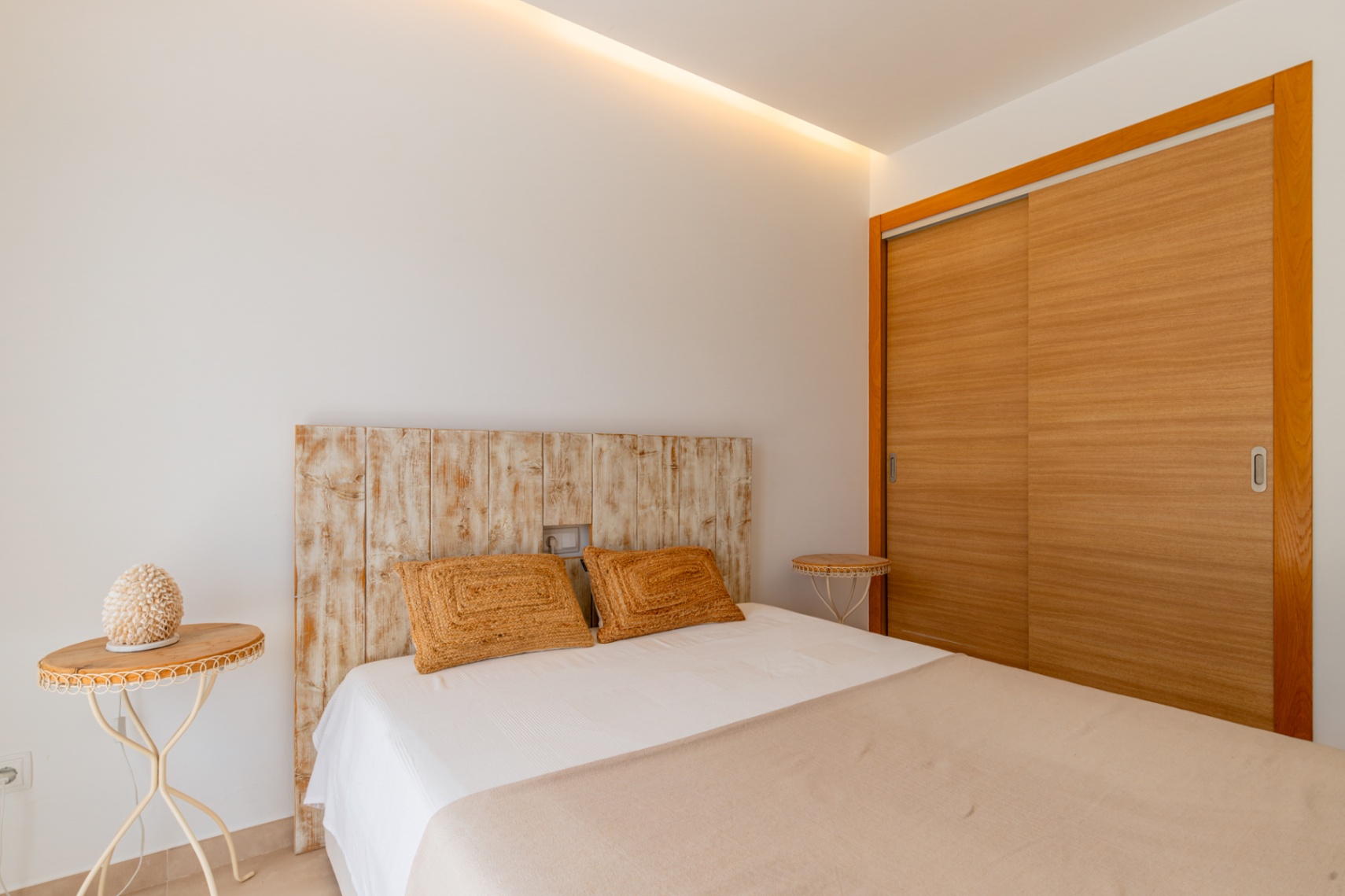 Chambre avec tête de lit en bois vieilli, armoire intégrée à portes coulissantes en bois clair et éclairage de plafond discret.