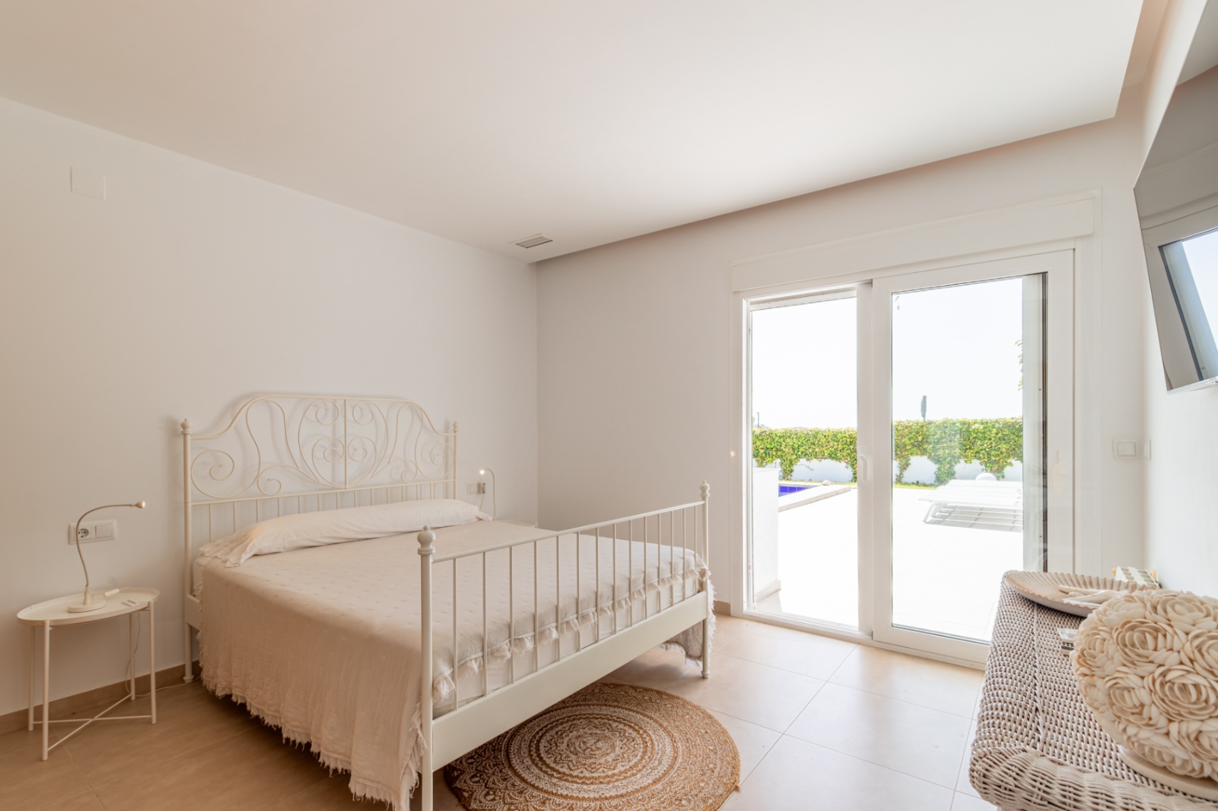 Chambre lumineuse avec lit en fer forgé blanc, sol carrelé et accès direct à la terrasse extérieure et à la piscine.