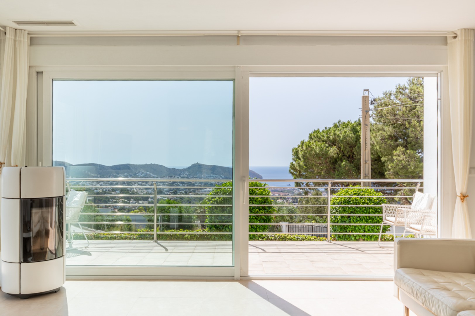 Espace de vie lumineux avec poêle à granulés moderne et grandes baies vitrées donnant sur une terrasse offrant des vues mer et paysagères.