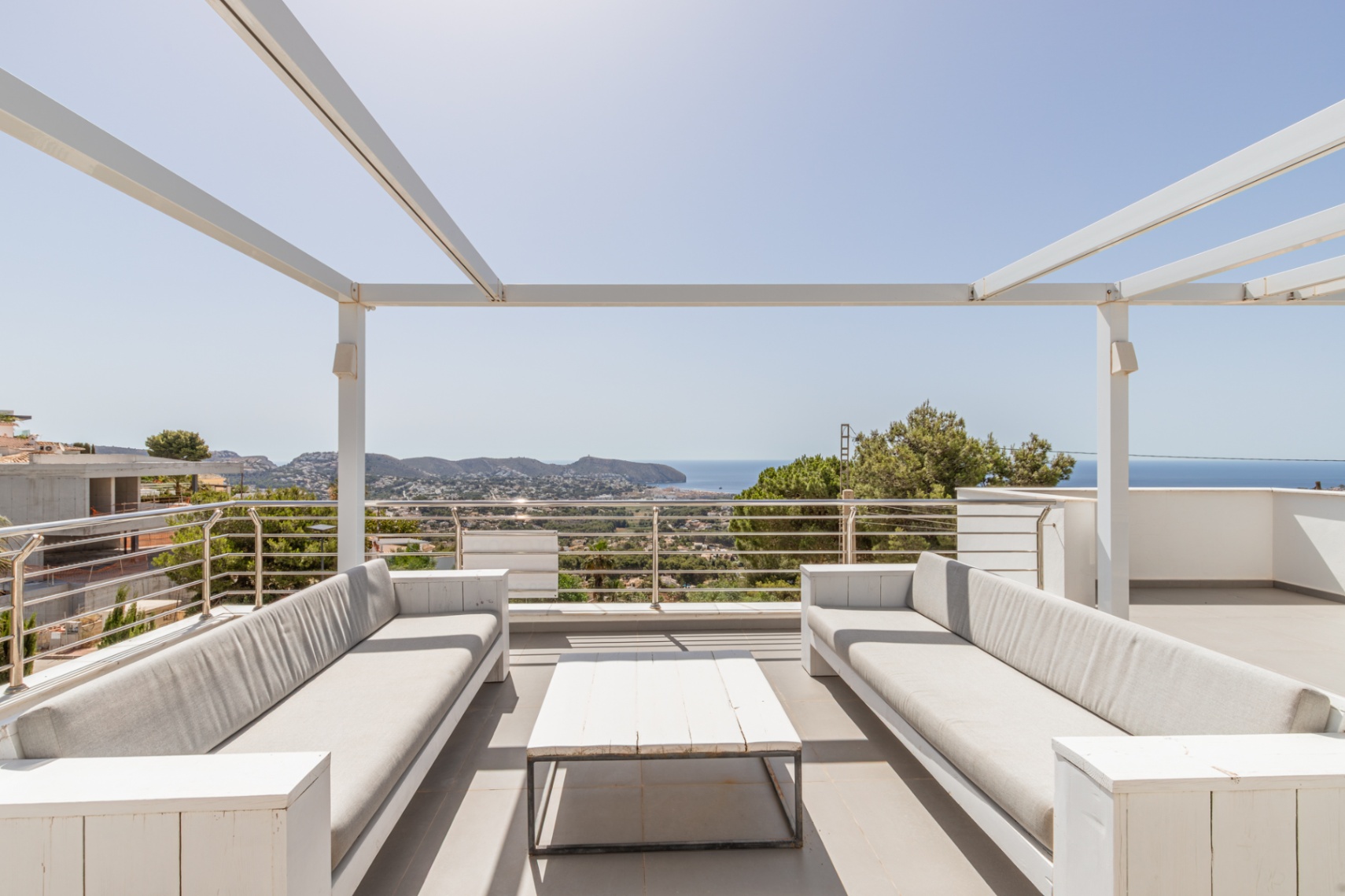 Solarium sur le toit avec pergola blanche, deux canapés d'extérieur confortables et une table basse, offrant des vues panoramiques sur la mer Méditerranée et la côte.