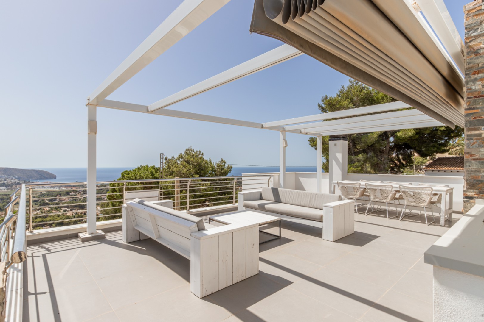 Vaste solarium sur le toit avec pergola blanche, store automatisé et coin salon offrant des vues panoramiques sur la mer.
