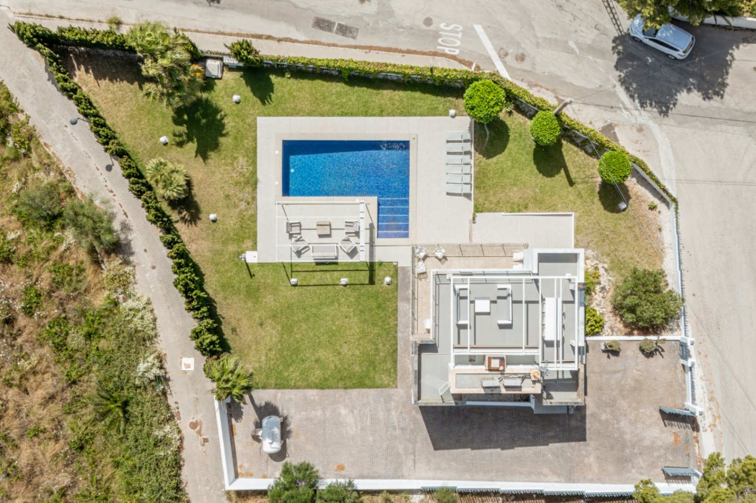 Vue aérienne de la propriété, révélant la piscine rectangulaire carrelée de bleu, les pelouses impeccables et une vaste zone de stationnement pavée. Le toit du bâtiment principal est visible.