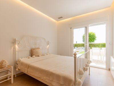 Chambre lumineuse avec lit en fer forgé blanc, éclairage LED indirect et accès direct à une terrasse privée avec jardin.