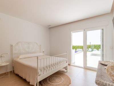 Chambre lumineuse avec lit en fer forgé blanc, sol carrelé et accès direct à la terrasse extérieure et à la piscine.