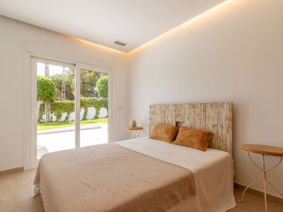 Chambre lumineuse avec tête de lit en bois rustique, éclairage intégré au plafond et accès direct à une terrasse jardin privée par des portes coulissantes.