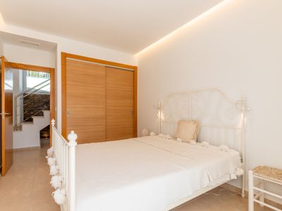Chambre lumineuse avec un lit en fer forgé blanc, une armoire intégrée en bois clair et un accès à l'escalier intérieur. Éclairage LED au plafond.