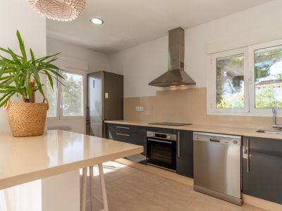 Cuisine moderne avec des armoires gris foncé, des plans de travail beige clair et des appareils en acier inoxydable. De grandes fenêtres offrent une lumière naturelle.