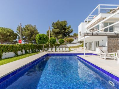 La piscine de 9x4 mètres aux carreaux de mosaïque bleus est entourée d'une terrasse claire avec chaises longues, jouxtant la villa blanche moderne avec parement en pierre et terrasse ombragée.