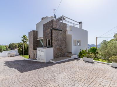 L'extérieur moderne de la villa combine parement en pierre, une large allée pavée et une rampe d'accès. Un réservoir de gaz Repsol est visible, avec un aménagement paysager méditerranéen.