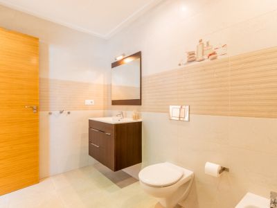 Salle de bain contemporaine avec carrelage clair, porte en bois, meuble-lavabo suspendu en bois foncé et miroir. WC mural avec plaque de chasse chromée.