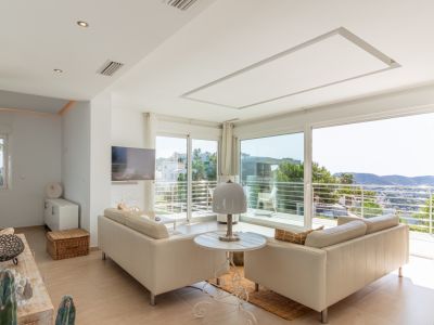 Vaste salon lumineux avec canapés clairs et grandes baies vitrées coulissantes donnant sur un balcon. Profitez de vues panoramiques sur les collines depuis cet espace doté d'une TV murale.