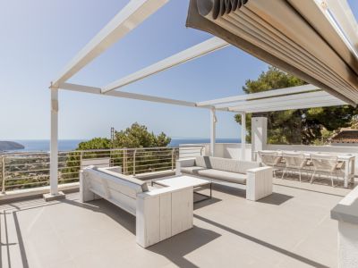 Vaste solarium sur le toit avec pergola blanche, store automatisé et coin salon offrant des vues panoramiques sur la mer.