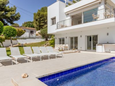 Vaste terrasse carrelée avec grande piscine en mosaïque bleue, six chaises longues blanches et coin repas extérieur. Une cuisine d'été intégrée avec réfrigérateur complète cet espace de loisirs.