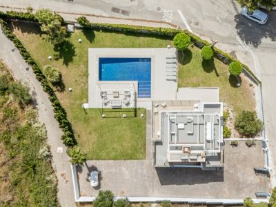 Vue aérienne de la propriété, révélant la piscine rectangulaire carrelée de bleu, les pelouses impeccables et une vaste zone de stationnement pavée. Le toit du bâtiment principal est visible.