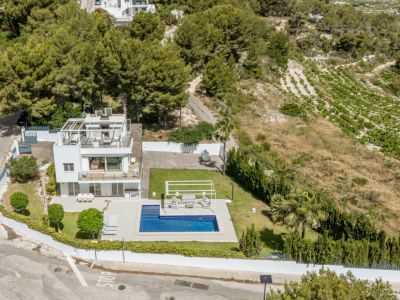 Vue aérienne de la villa blanche à trois niveaux, avec piscine, pelouse soignée et solarium sur le toit avec pergola. Entourée de pins et de vignobles.