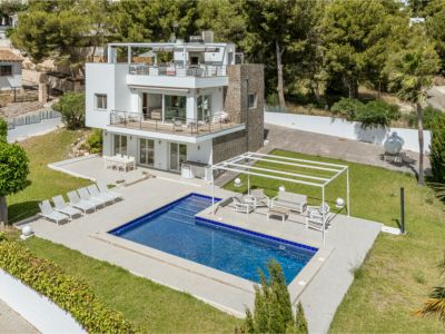 Vue aérienne de la villa moderne à plusieurs niveaux, avec piscine rectangulaire, vastes terrasses salon et salle à manger, et pelouses soignées, entourée de végétation luxuriante.