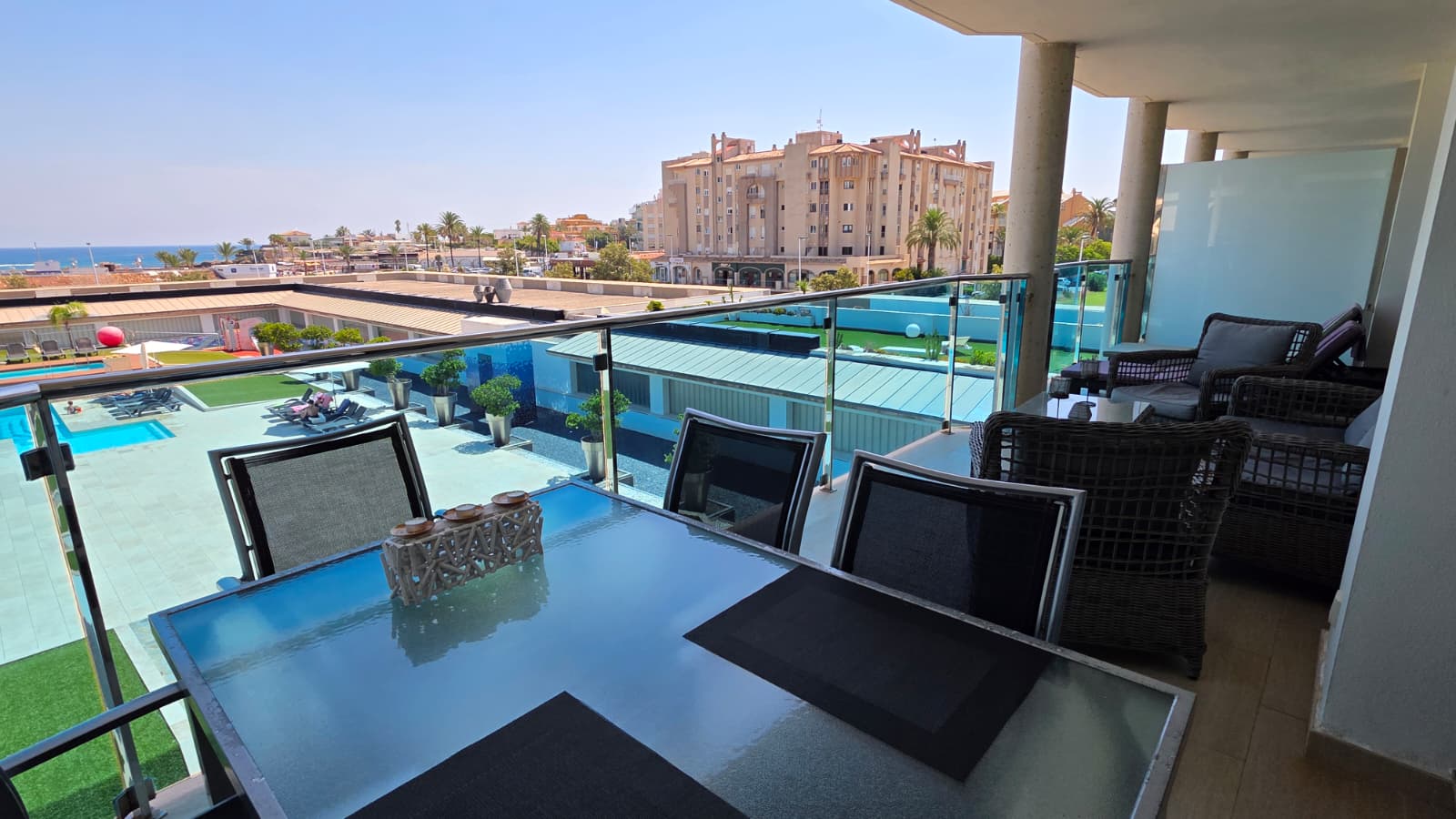Grande terrasse aménagée avec une table à manger en verre et un salon en rotin, offrant une vue dégagée sur la piscine résidentielle et la mer Méditerranée.