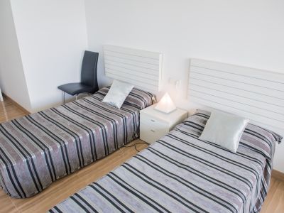 Chambre avec deux lits simples, têtes de lit blanches à lattes et literie rayée. Une lampe pyramidale éclaire la table de chevet située entre les lits.