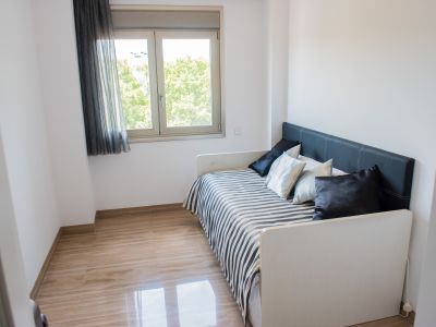 Chambre individuelle avec lit de jour, tête de lit noire capitonnée et literie rayée. Le sol en marbre clair poli et la fenêtre offrent une vue sur la verdure.