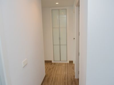 Couloir intérieur aux murs blancs et sol carrelé effet marbre veiné. Au fond, une armoire encastrée avec portes en verre dépoli et cadre argenté, éclairage encastré.