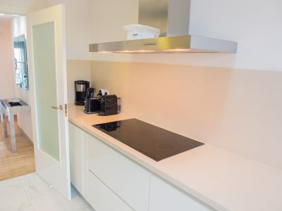 Cuisine moderne avec plan de travail clair, plaque à induction noire et hotte aspirante en acier inoxydable. Le sol carrelé effet marbre s'ouvre sur un espace avec parquet.