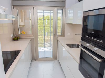 Cuisine moderne en couloir avec des armoires blanches laquées, des plans de travail clairs et des appareils Siemens intégrés. Une porte vitrée double battant offre lumière naturelle et accès au balcon.