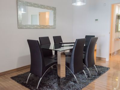 Espace repas contemporain avec table en verre et six chaises en similicuir noir. Un miroir vieilli et un tapis gris complètent le sol en marbre poli.