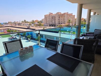 Grande terrasse aménagée avec une table à manger en verre et un salon en rotin, offrant une vue dégagée sur la piscine résidentielle et la mer Méditerranée.