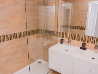 Salle de bain moderne avec douche à l'italienne vitrée et double vasque. Les carreaux muraux beiges sont rehaussés d'une bande décorative en mosaïque.