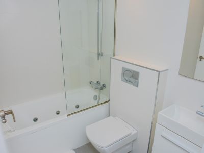 Salle de bain moderne blanche avec baignoire à jets intégrés, paroi de douche en verre, WC suspendu et lavabo rectangulaire. Carrelage mural blanc et robinetterie chromée.