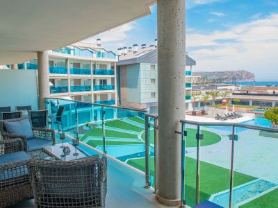 Vaste terrasse privée aménagée avec mobilier d'extérieur en rotin, offrant une vue directe sur les piscines communes et la mer Méditerranée. Garde-corps en verre.