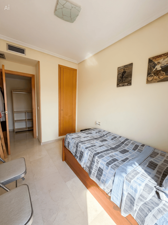 Chambre individuelle avec lit en bois, sol effet marbre clair et armoire intégrée. Un dressing ouvert adjacent et une bouche de climatisation sont visibles.