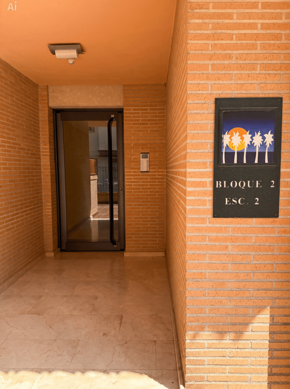 L'entrée du Bloc 2, Escalier 2, présente une façade en briques, un sol en marbre clair et une porte vitrée avec interphone. Une plaque décorative indique le numéro du bloc.