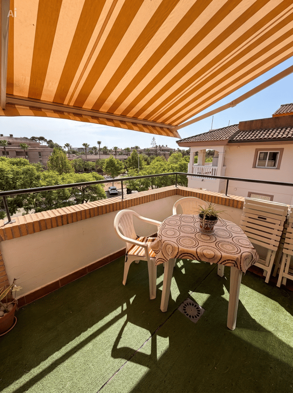 Terrasse extérieure avec gazon synthétique, mobilier de jardin en plastique et store banne rayé. Vues sur la verdure et les résidences.